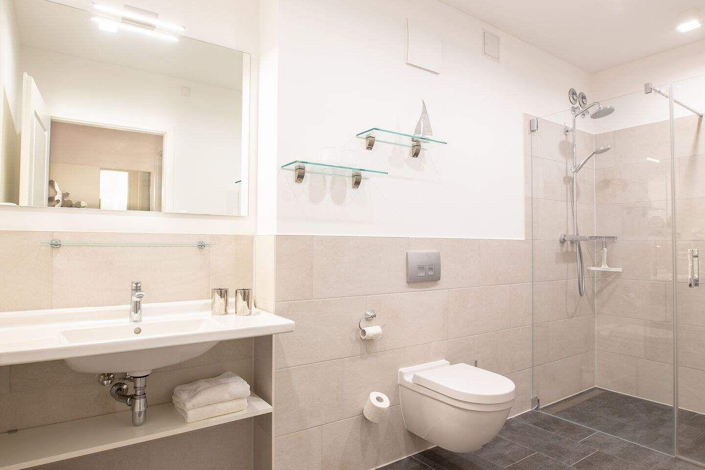 Badezimmer mit Dusche, Waschbecken und WC. Glasregale und Spiegel.