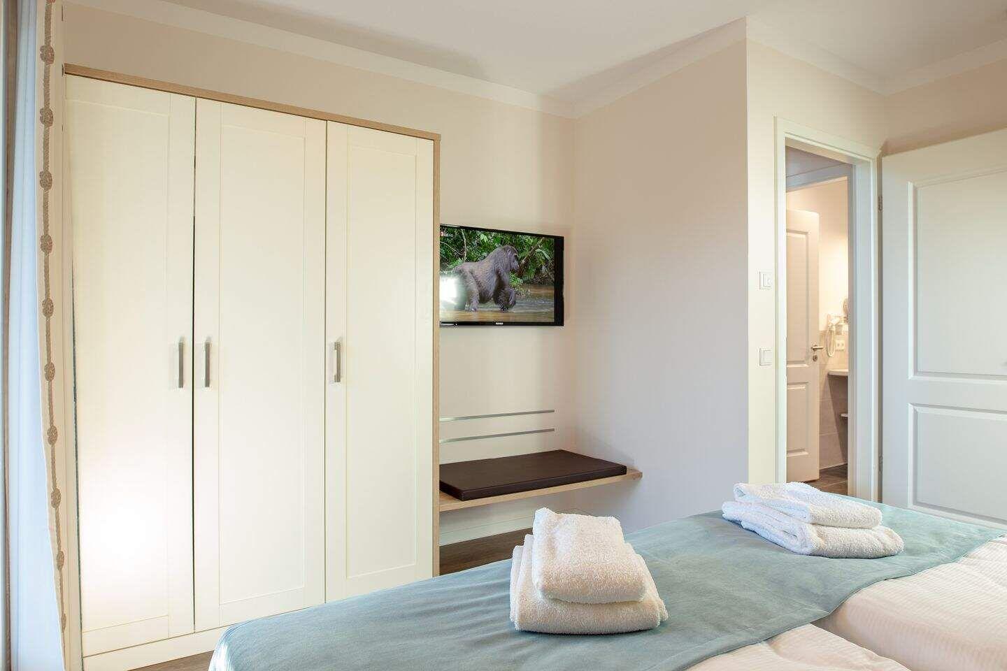 Schlafzimmer mit Bett, Kleiderschrank und Fernseher. Blick in das Bad.
