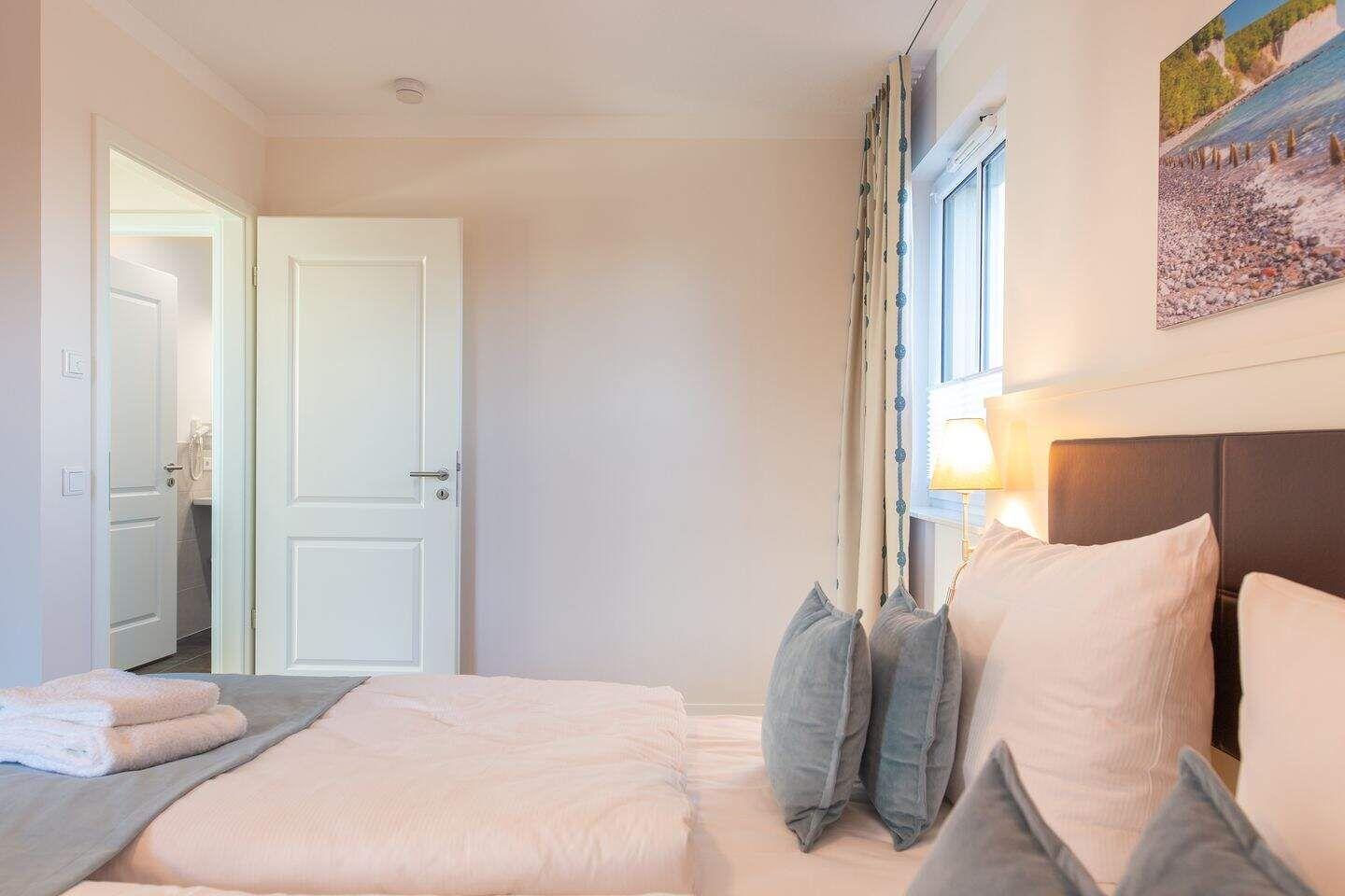 Schlafzimmer mit Bett, Fenster und Bild an der Wand. Tür führt in angrenzenden Raum.