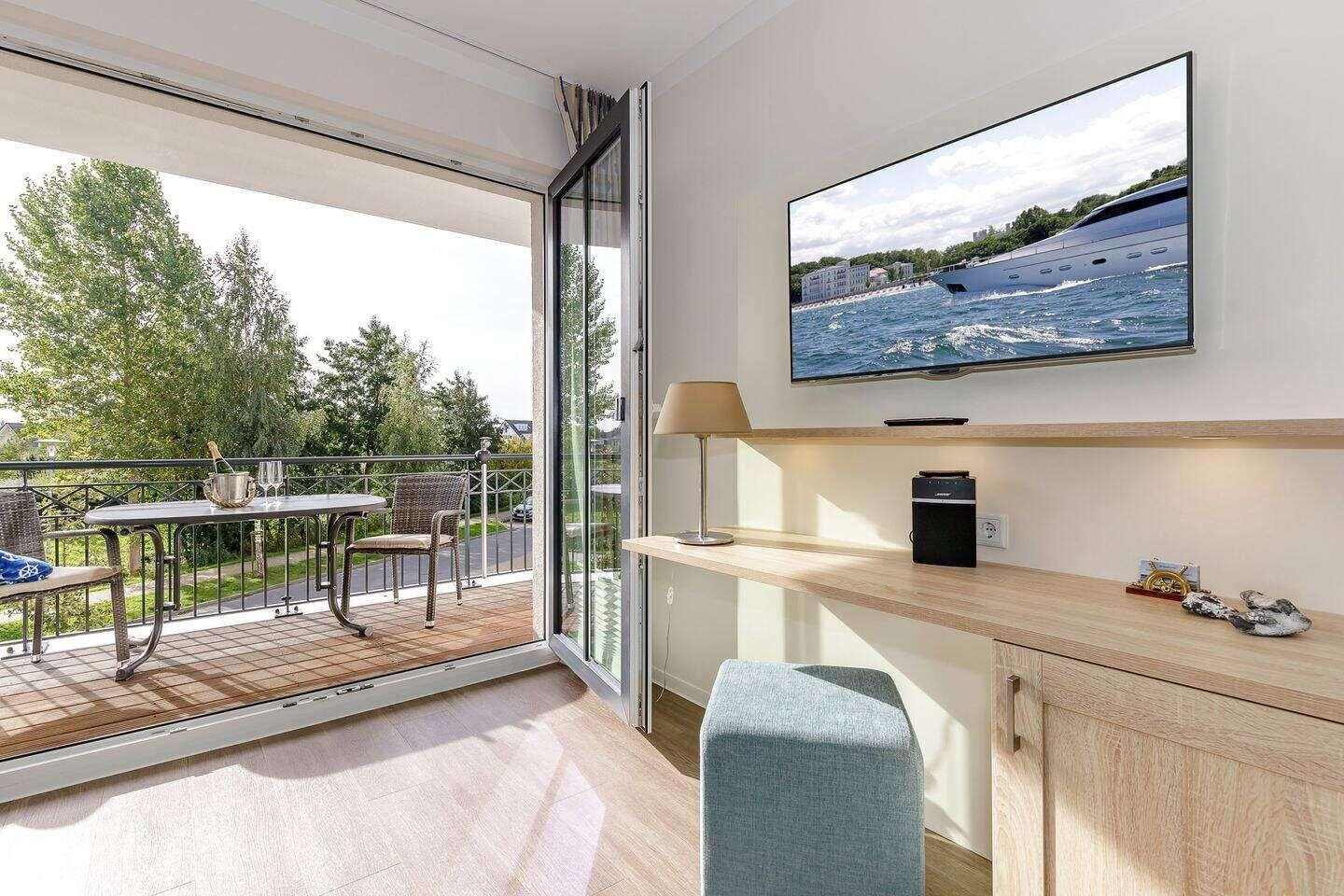Wohnraum mit TV und Balkon mit Tisch und Stühlen.