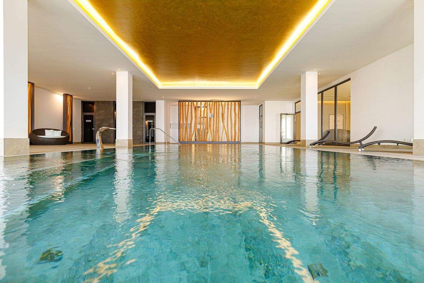 Großer Innenpool mit Liegen und goldfarbenem Deckenlicht.