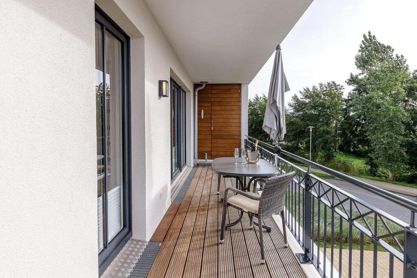 Terrasse mit Tisch, Stühlen und Sonnenschirm. Holzdielen und Metallgeländer.