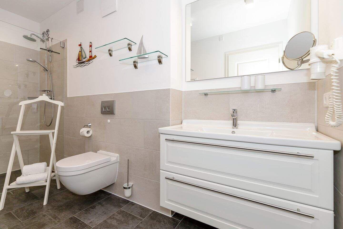 Badezimmer mit Dusche, Waschbecken und Toilette. Weiße Einbauschränke und Spiegel.