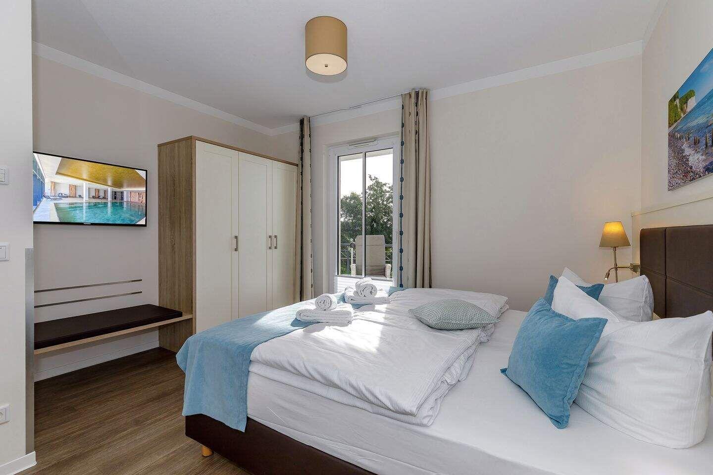 Schlafzimmer mit Bett, Kleiderschrank und TV. Fenster mit Blick auf Balkon.