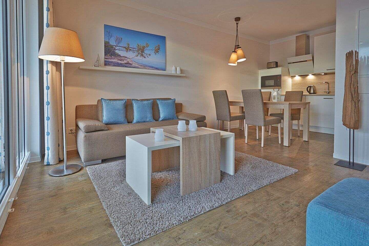 Wohnbereich mit Sofa, Couchtisch und Essbereich. Küchenzeile mit Kochfeld und Spüle.