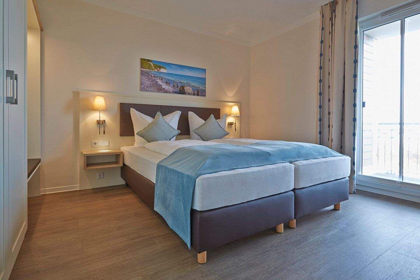 Schlafzimmer mit Doppelbett, Bild an der Wand und Balkontür.