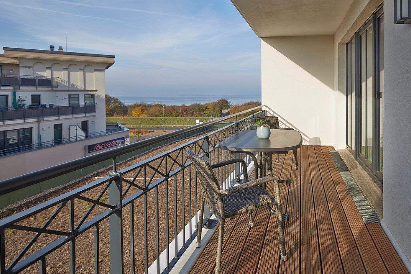 Terrasse mit Tisch und Stühlen, Blick auf Meer und Gebäude.