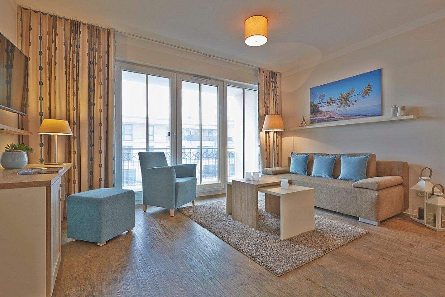 Wohnzimmer mit Sofa, Sessel und großen Fenstern.