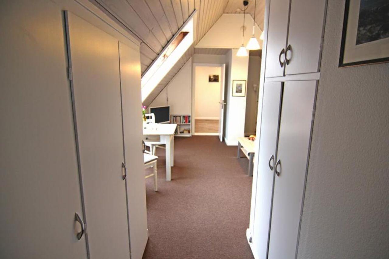 Dachflur mit weißen Schränken, Schreibtisch unterm Dachfenster und Holzdecke.