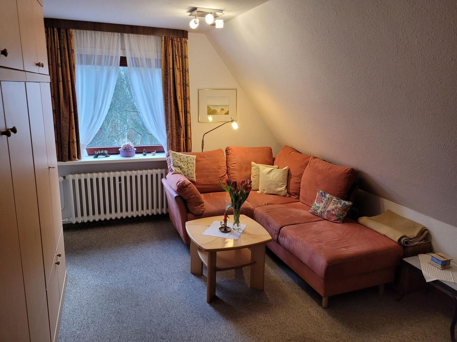 Wohnzimmer mit rotem Ecksofa unter Dachschräge, Couchtisch und Fenster.