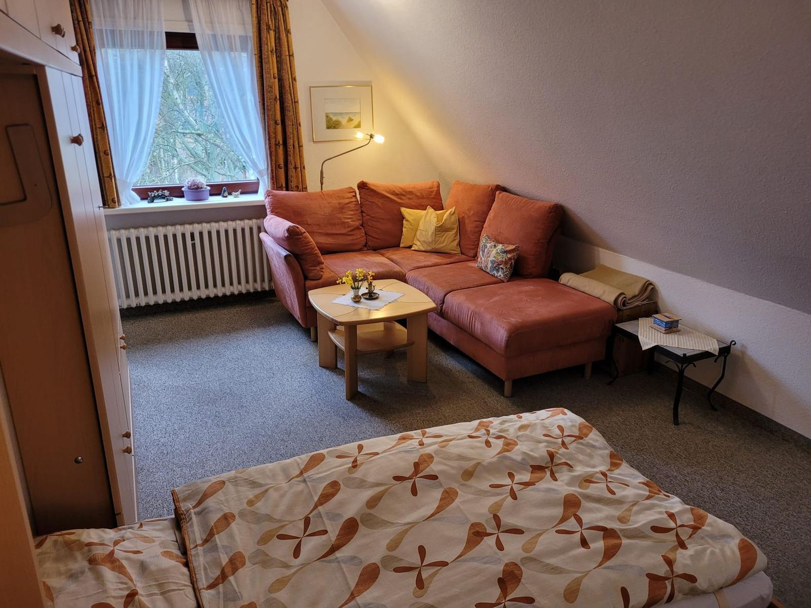 Wohnzimmer mit rotem Ecksofa, Couchtisch und Bett im Vordergrund.