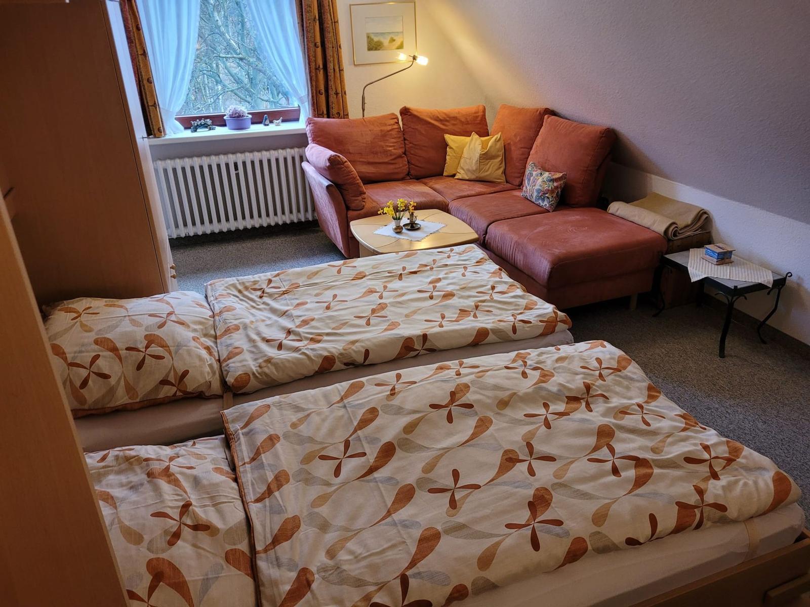Schlaf- und Wohnbereich mit zwei Betten, Ecksofa und Fenster unterm Dach.