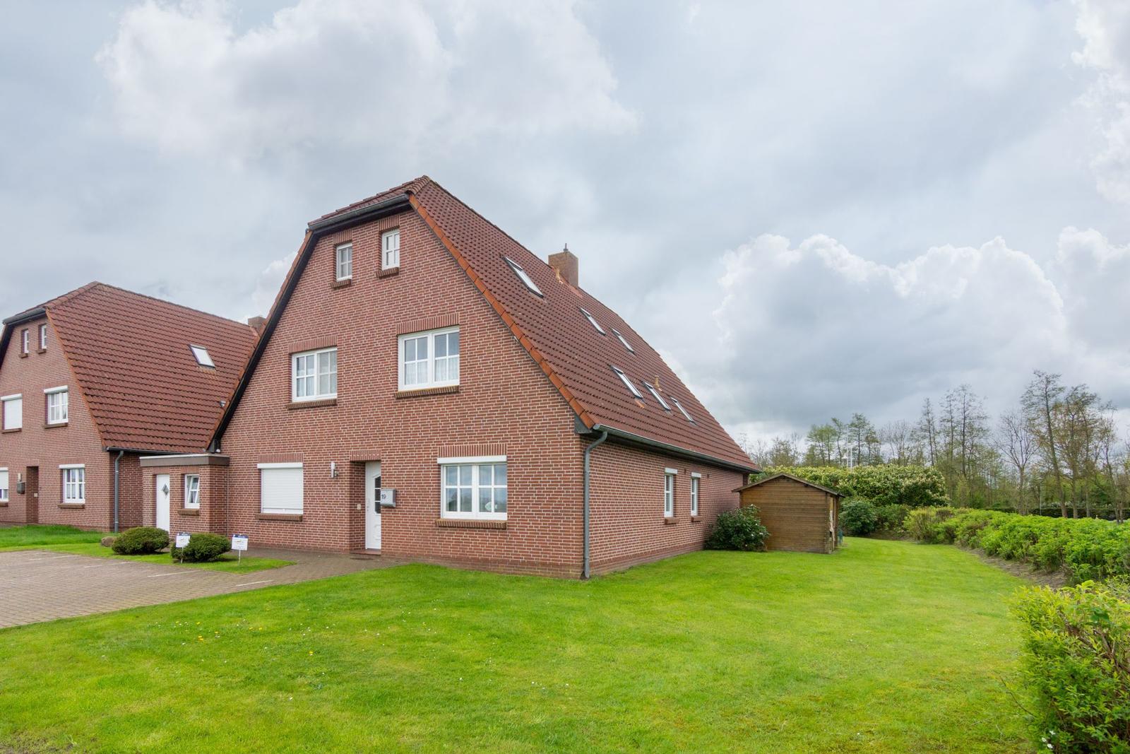 Haus mit rotem Dach und Garten unter bewölktem Himmel.