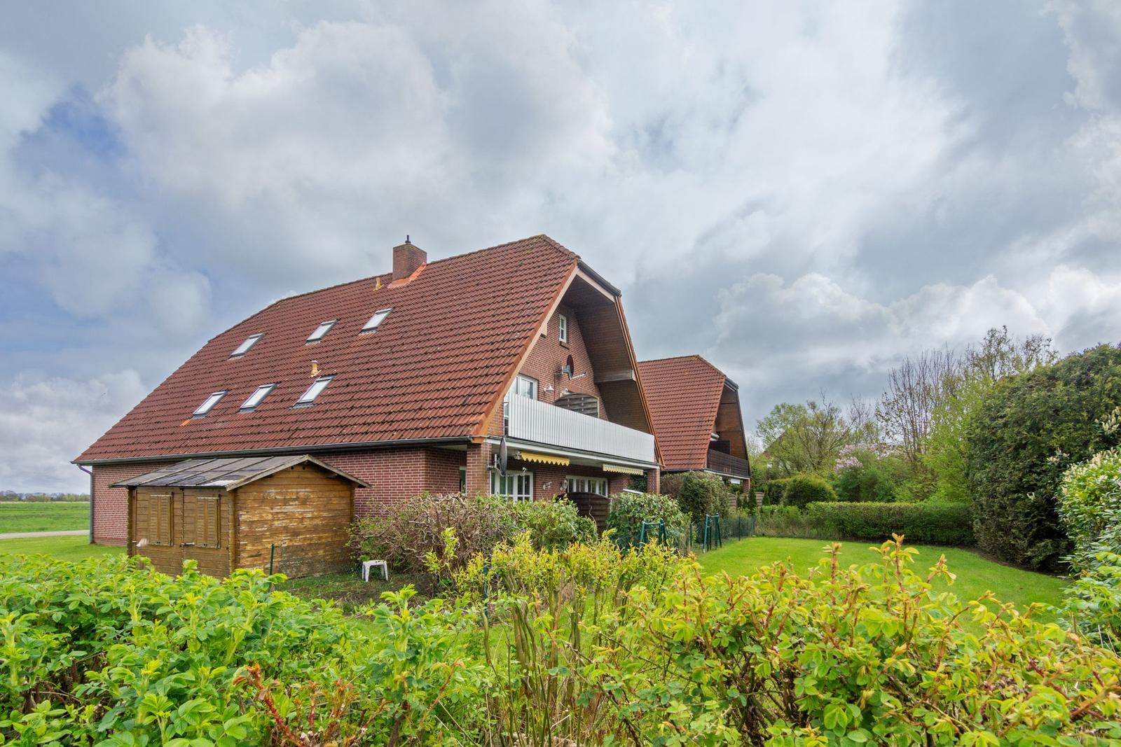Ein zweistöckiges Haus mit Balkon, Garten und Satellitenschüsseln unter blauem Himmel.