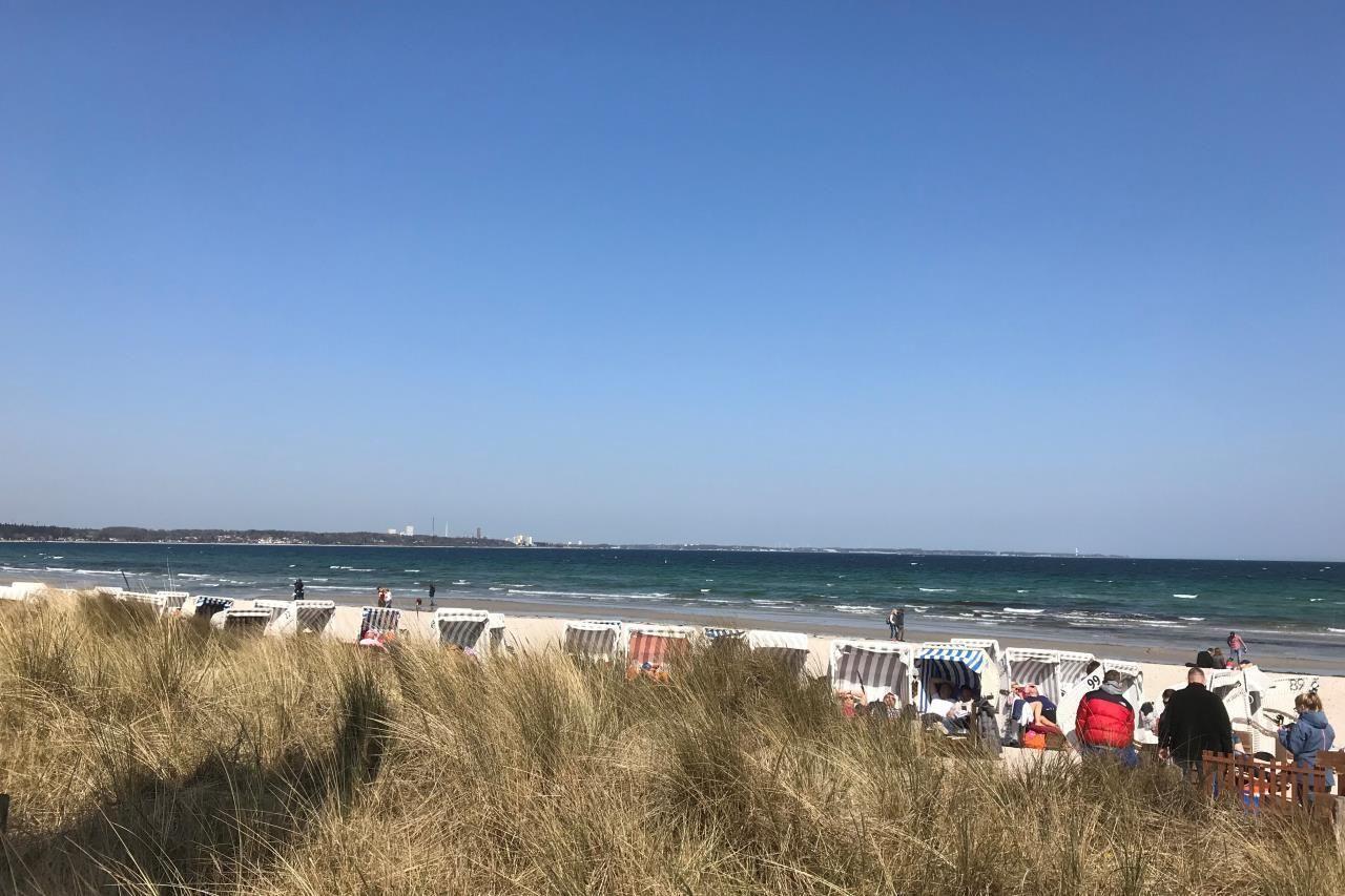 Strand mit Liegestühlen und Menschen. Meer und Himmel sind blau.