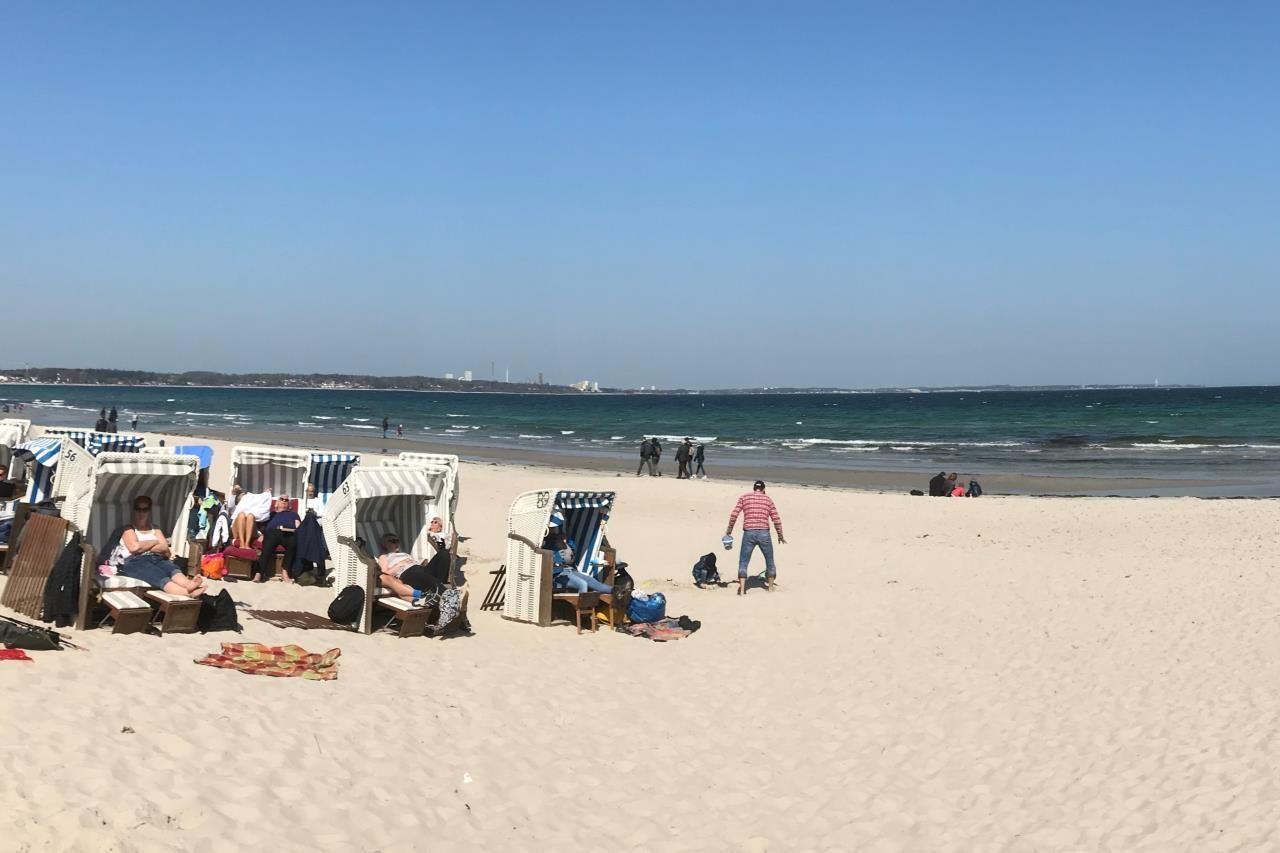 Strand mit weißen Sand, Menschen, Wellen und Pier im Hintergrund.