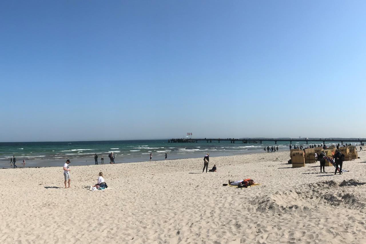 Hafenbrücke mit Menschen und einem weißen Boot im Meer.