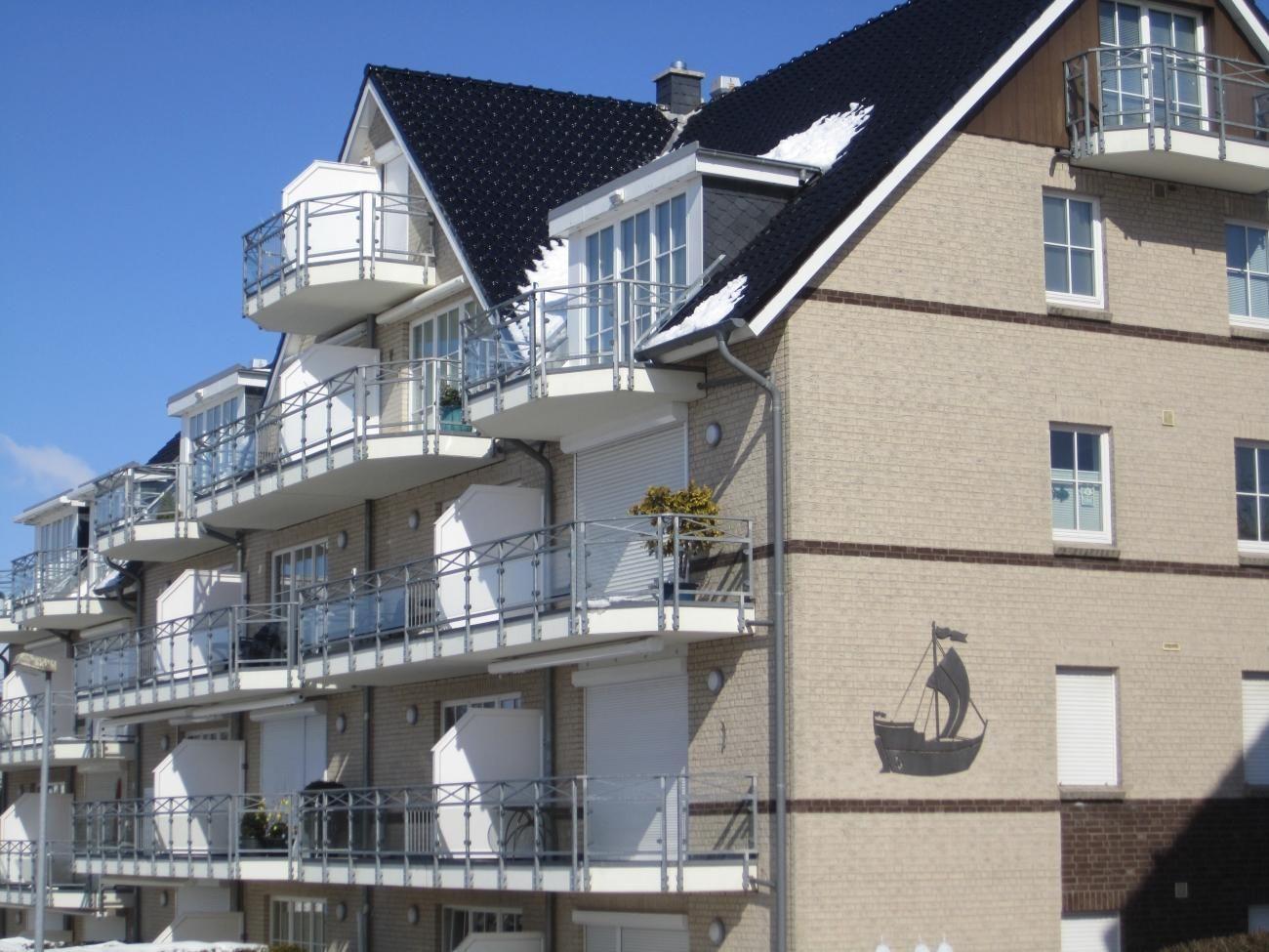 Strandpromenade mit Sandstrand, Wellen und Strandkörben unter blauem Himmel.