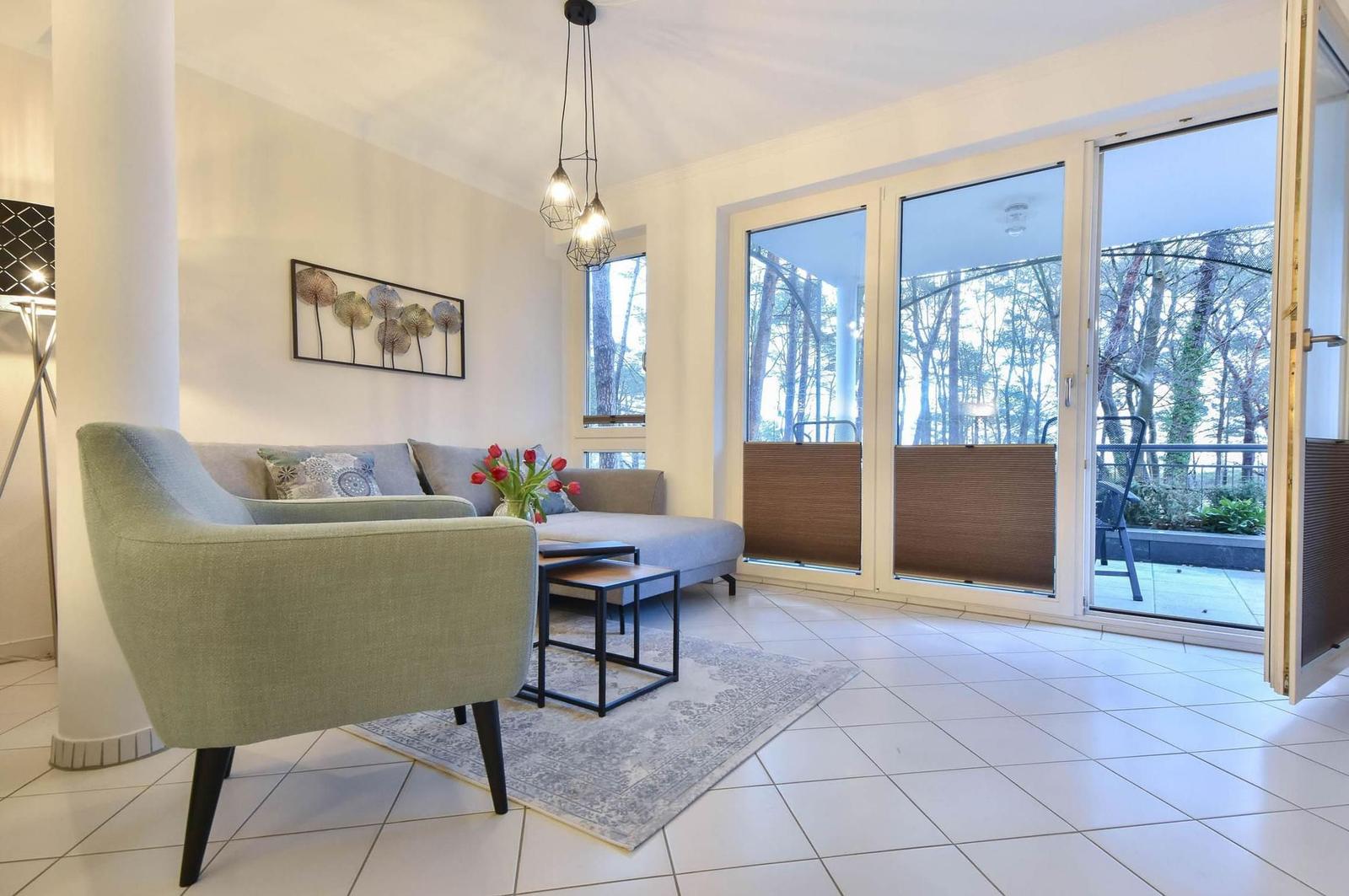 Wohnbereich mit Sofa, Sessel und Küchenbereich im Hintergrund.