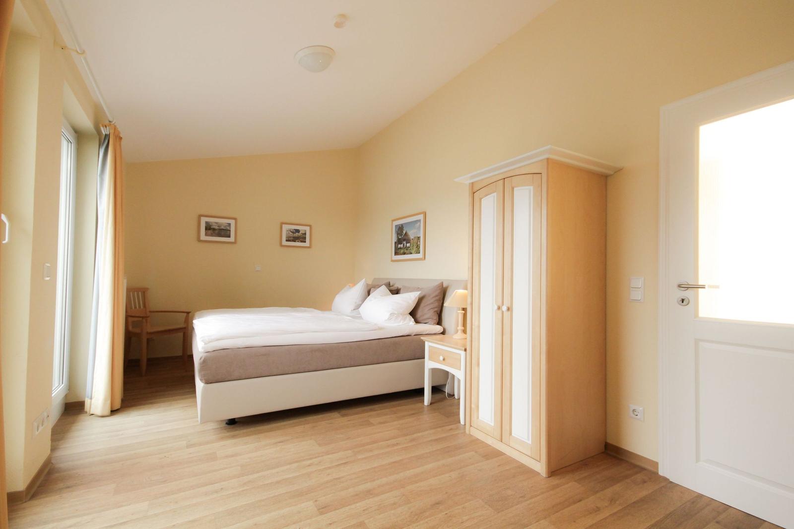 Schlafzimmer mit Balkon und Blick auf Wasser. Holzboden, Bett, Schrank und Tisch.