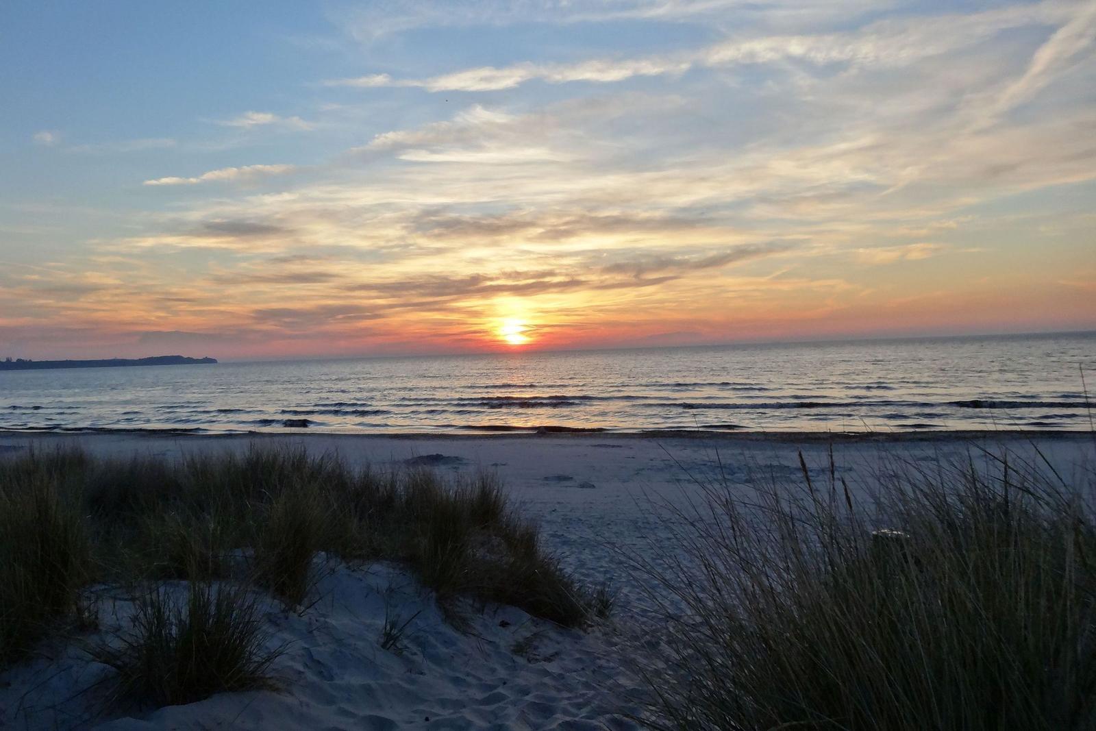 Sonnenuntergang über dem Meer mit orangefarbenem Himmel und glitzerndem Wasser.