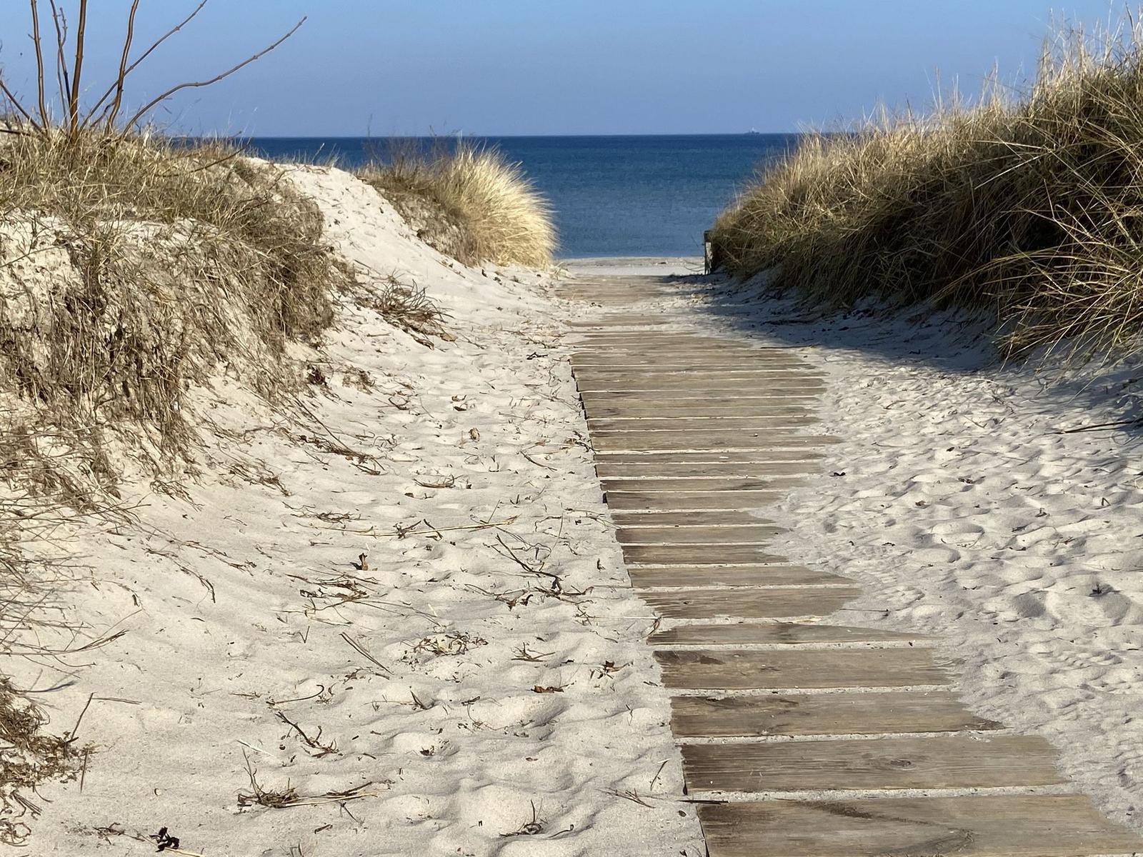 Weg durch Sanddünen zum Meer unter blauem Himmel mit Wolken.