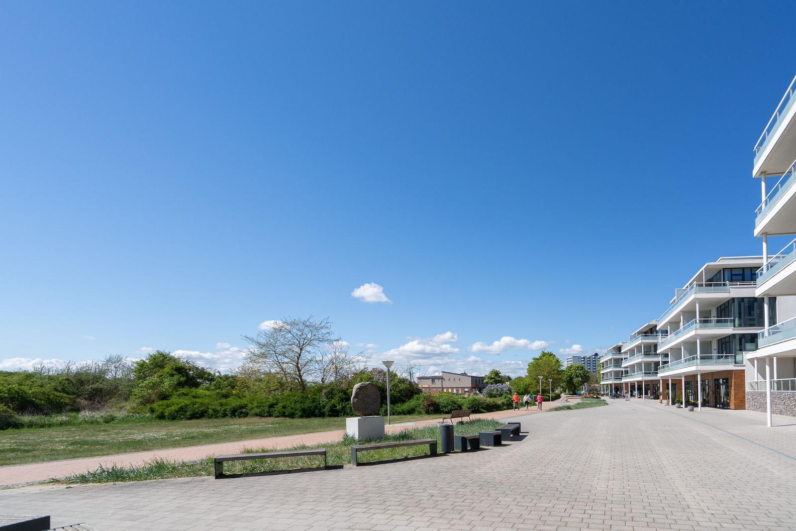 Modernes Mehrfamilienhaus mit Spielplatz und grüner Umgebung unter blauem Himmel.