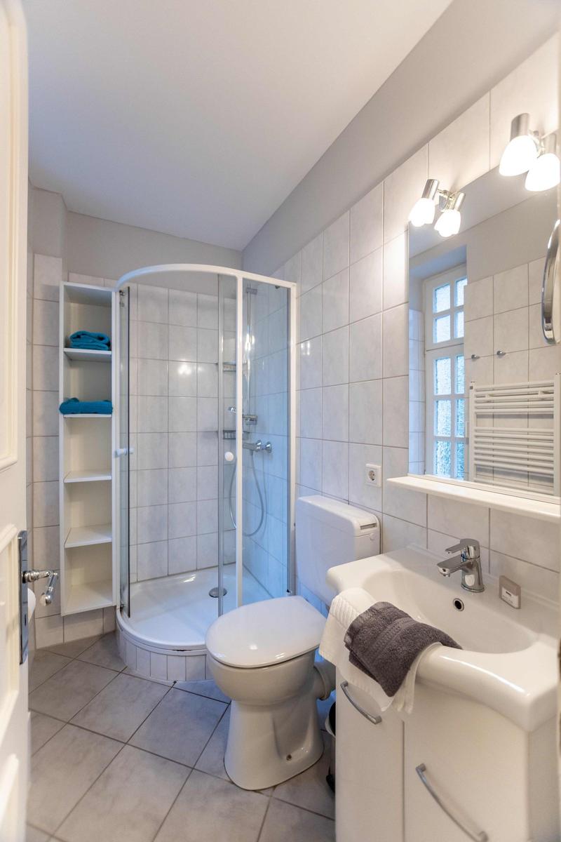 Badezimmer mit Toilette, Waschbecken und Spiegel. Holzboden im angrenzenden Raum.