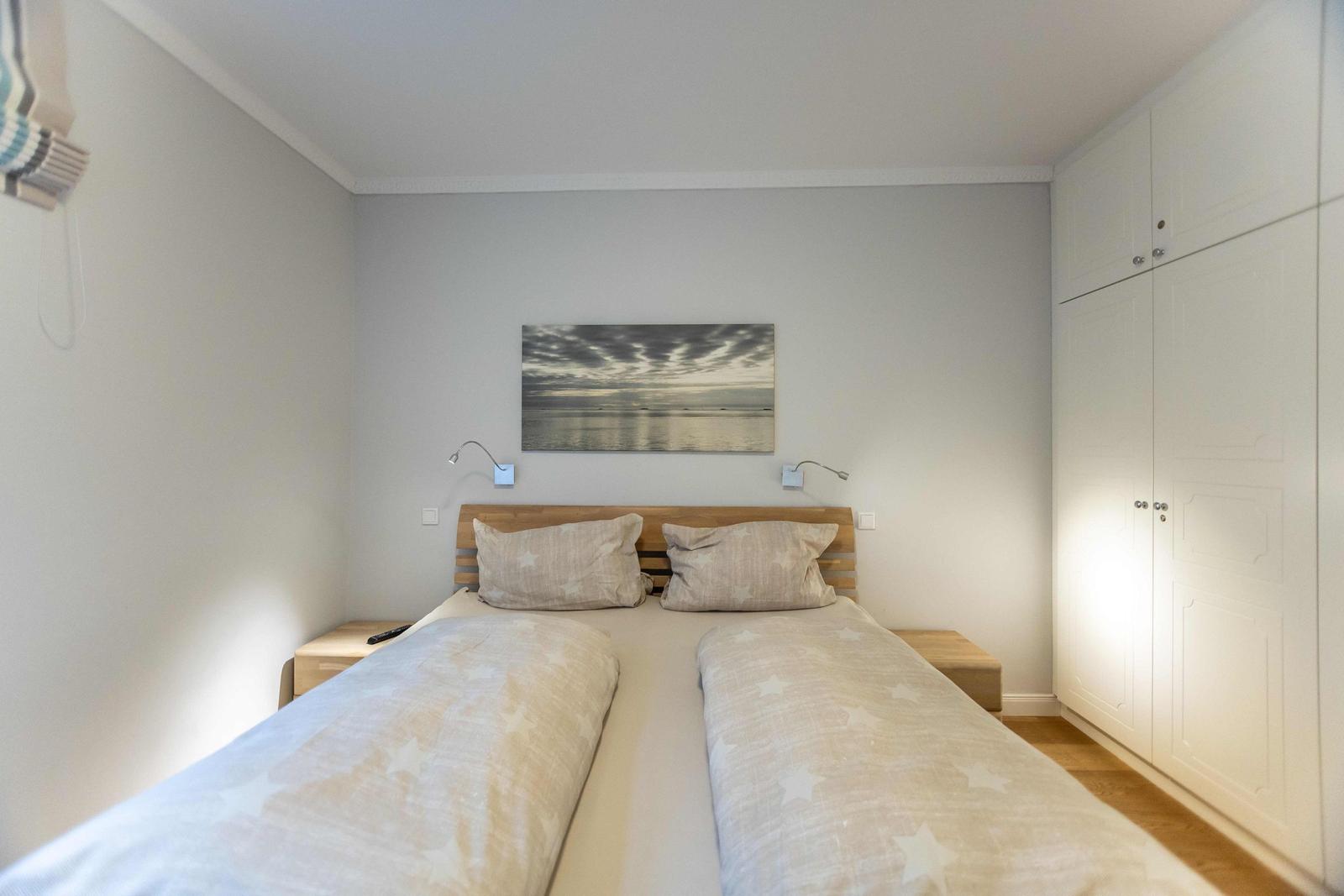 Schlafzimmer mit Doppelbett, Holzboden und Fenster mit Vorhang.