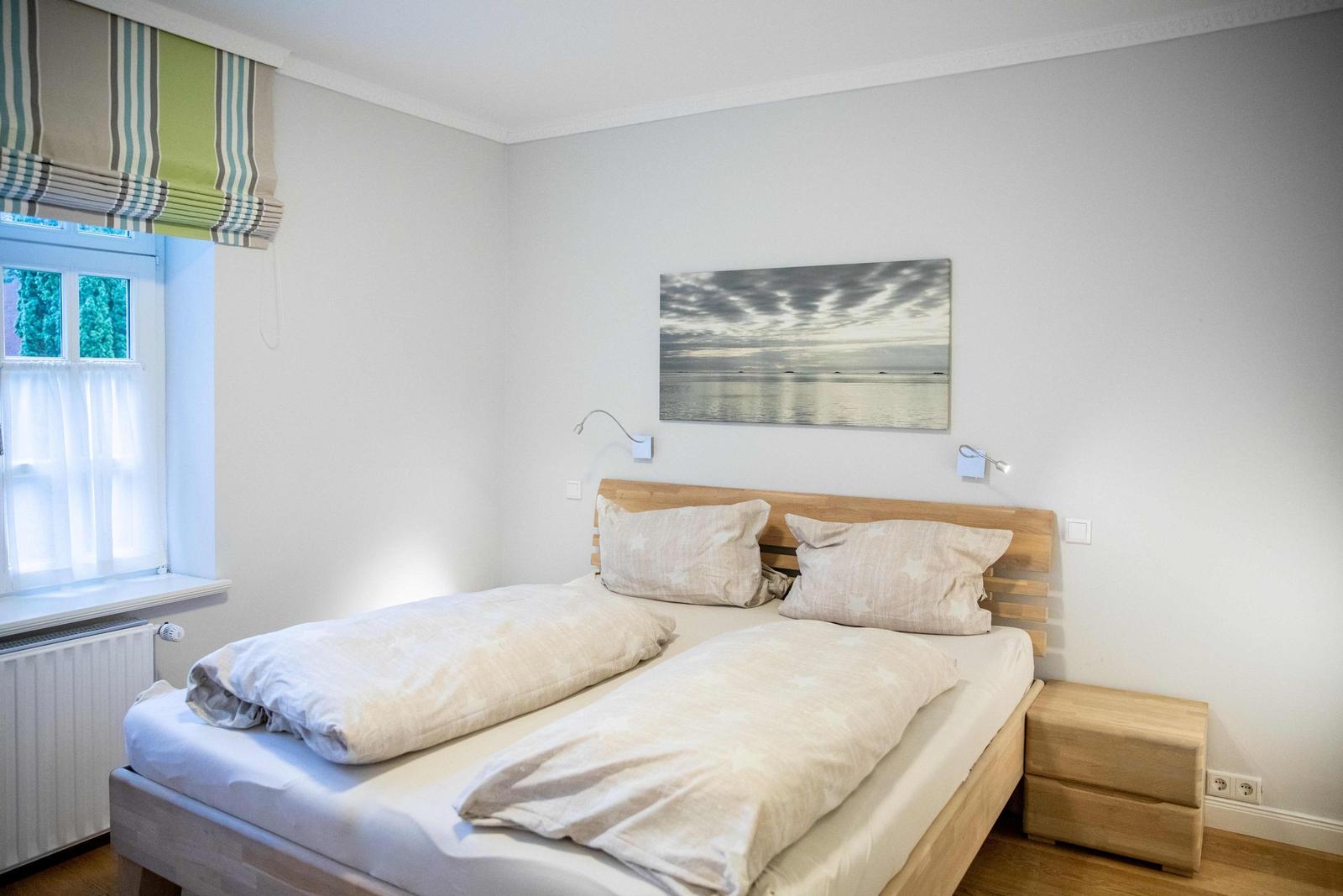 Schlafzimmer mit Doppelbett, Holzkopfteil und Wandbild. Weiße Schränke an der Wand.