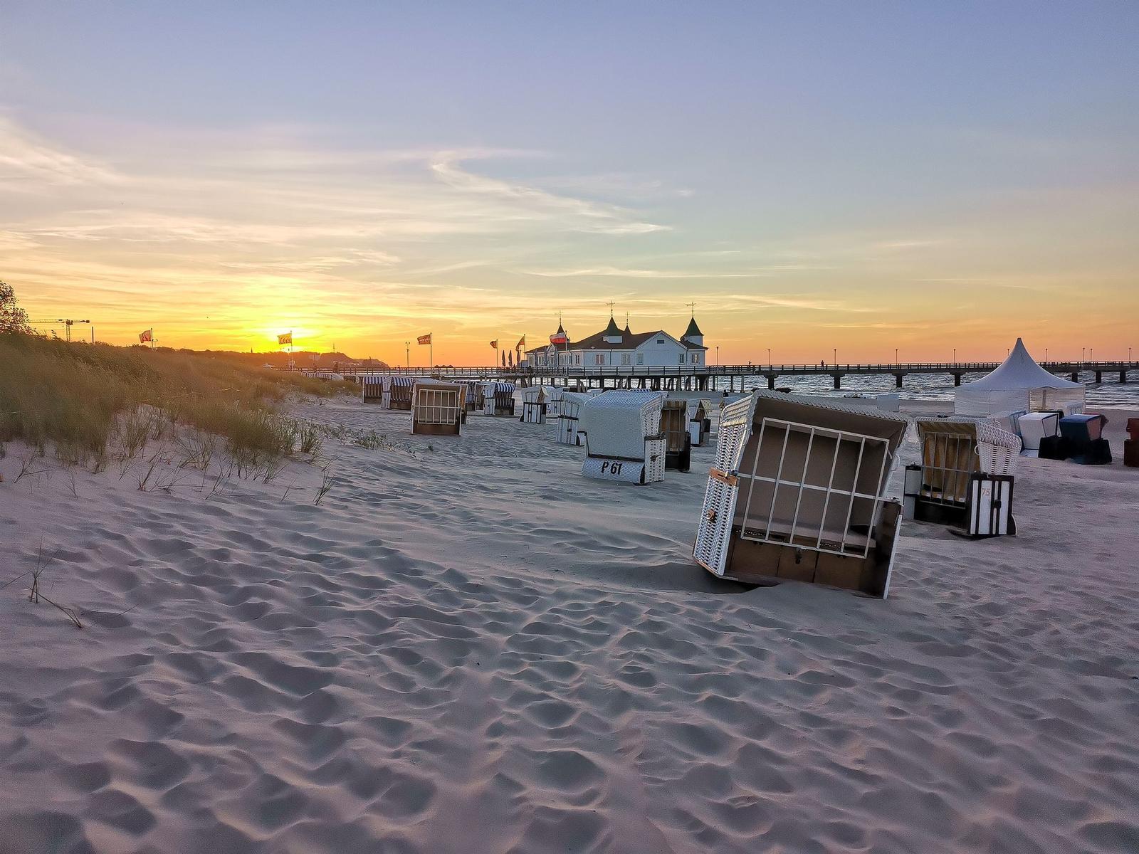 Sonne geht über Meer, Sanddünen mit Gras im Vordergrund.