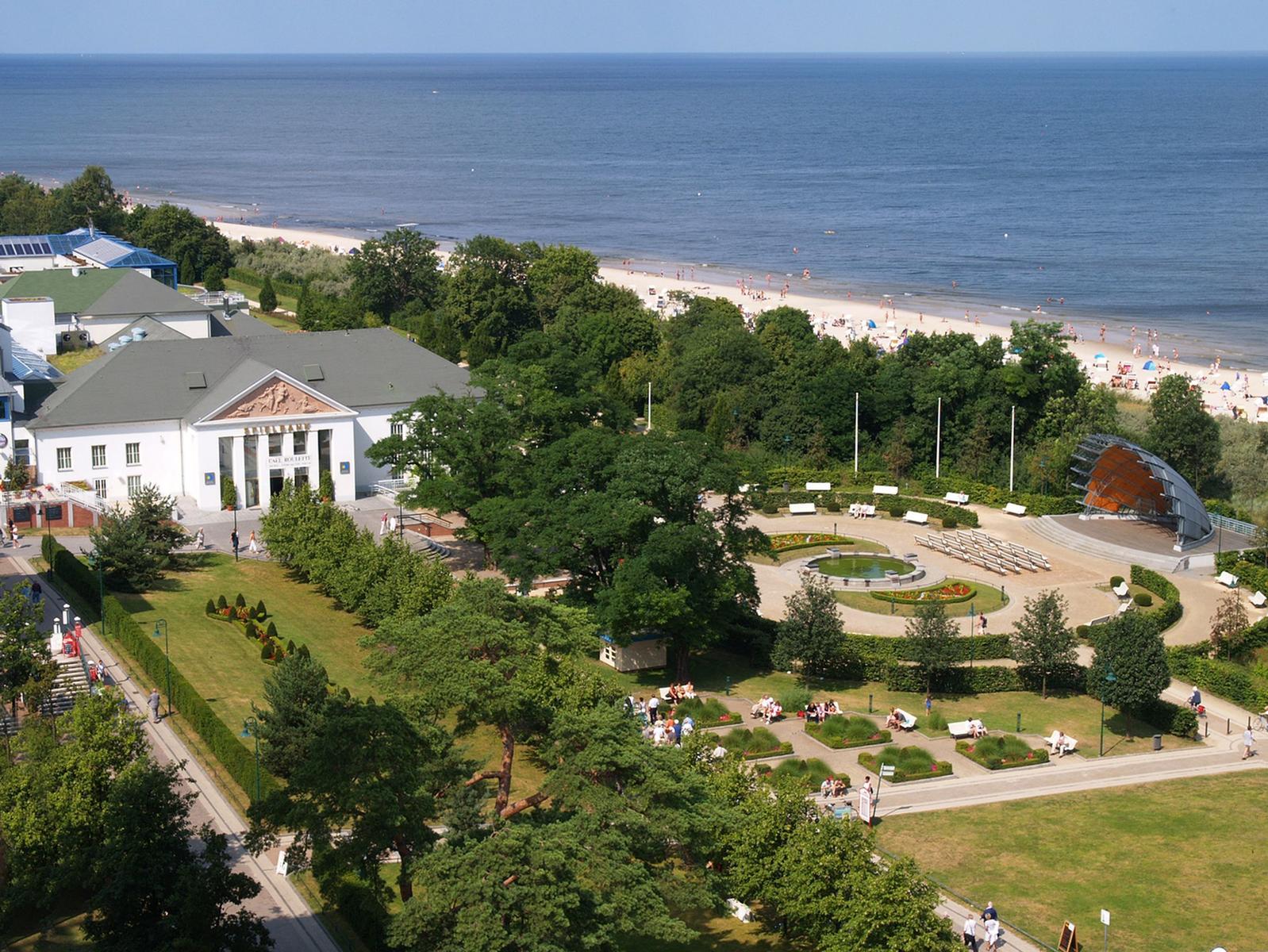 Hochgelegenes Strandhaus mit Terrasse, roten Sonnenschirmen und Flaggen an sonnigem Tag.