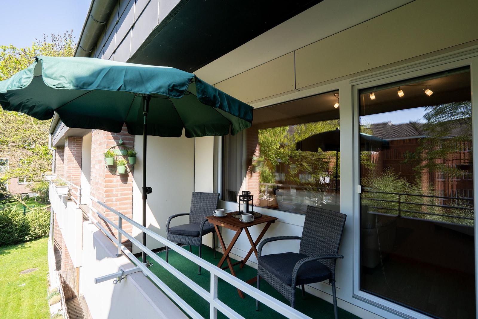 Balcony with green umbrella, table, chairs, and view of trees and buildings.