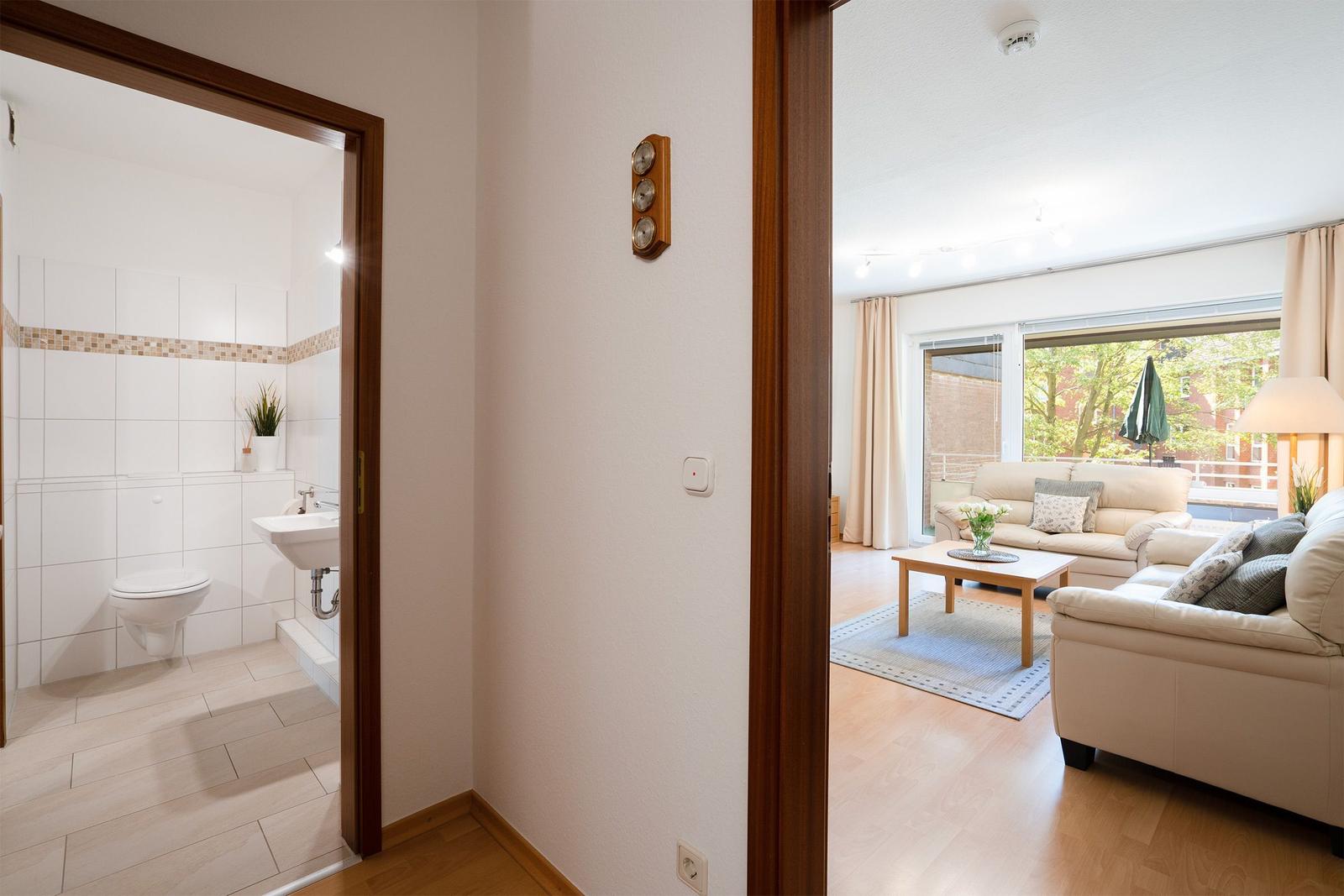 Badezimmer mit Toilette, Waschbecken und Spiegel. Wandverkleidung mit Mosaikstreifen.