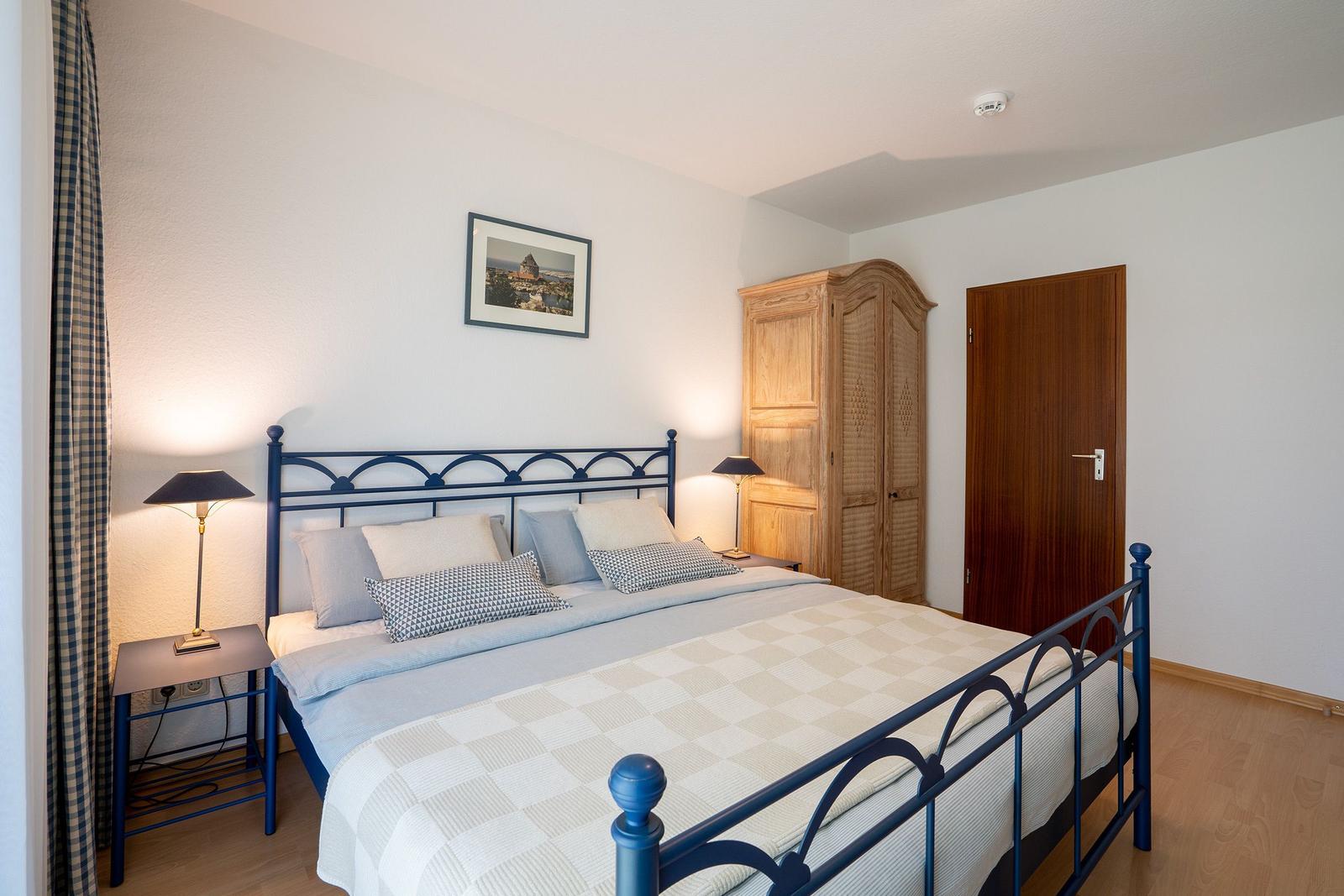 Schlafzimmer mit Bett, Nachttischen und Kleiderschrank. Tür führt in die Dusche.