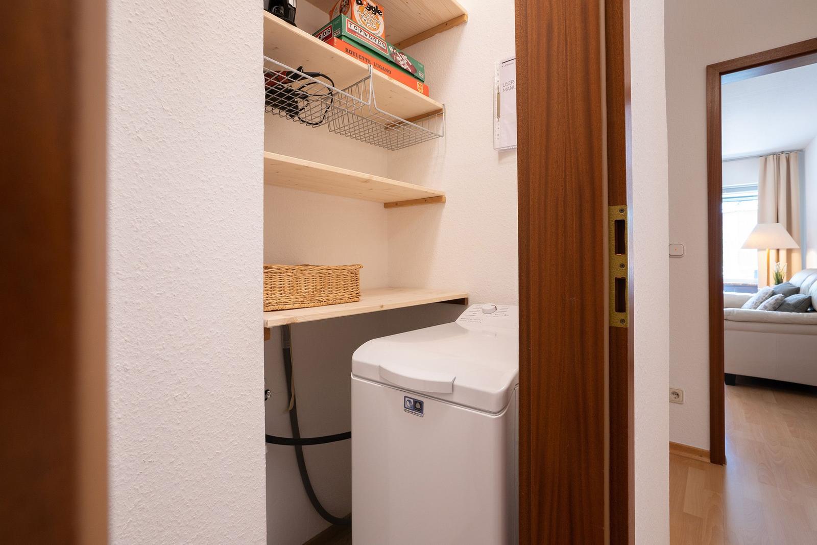 Hausgang mit Holztreppe und zwei Türen. Eine Tür hat ein Willkommen-Schild.