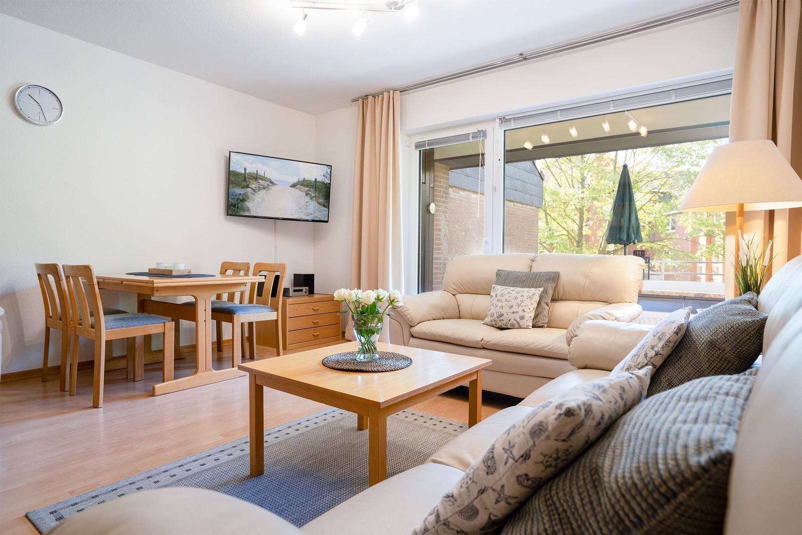 Wohnzimmer mit Essbereich, Sofa, Couch und TV. Balkon mit Blick auf Grün.