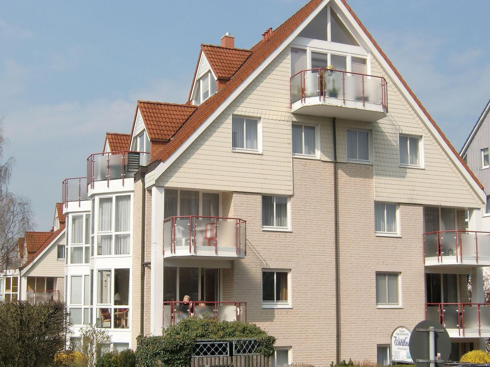 Straße mit Wohnhäusern und parkenden Autos unter blauem Himmel.