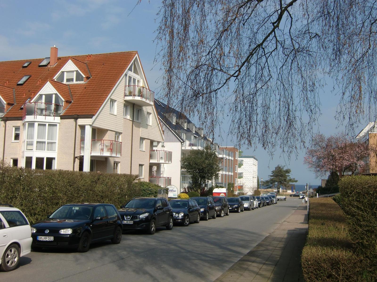 Ein gepflasterter Weg führt durch Gras zu einem Strand mit Wasser und Menschen.
