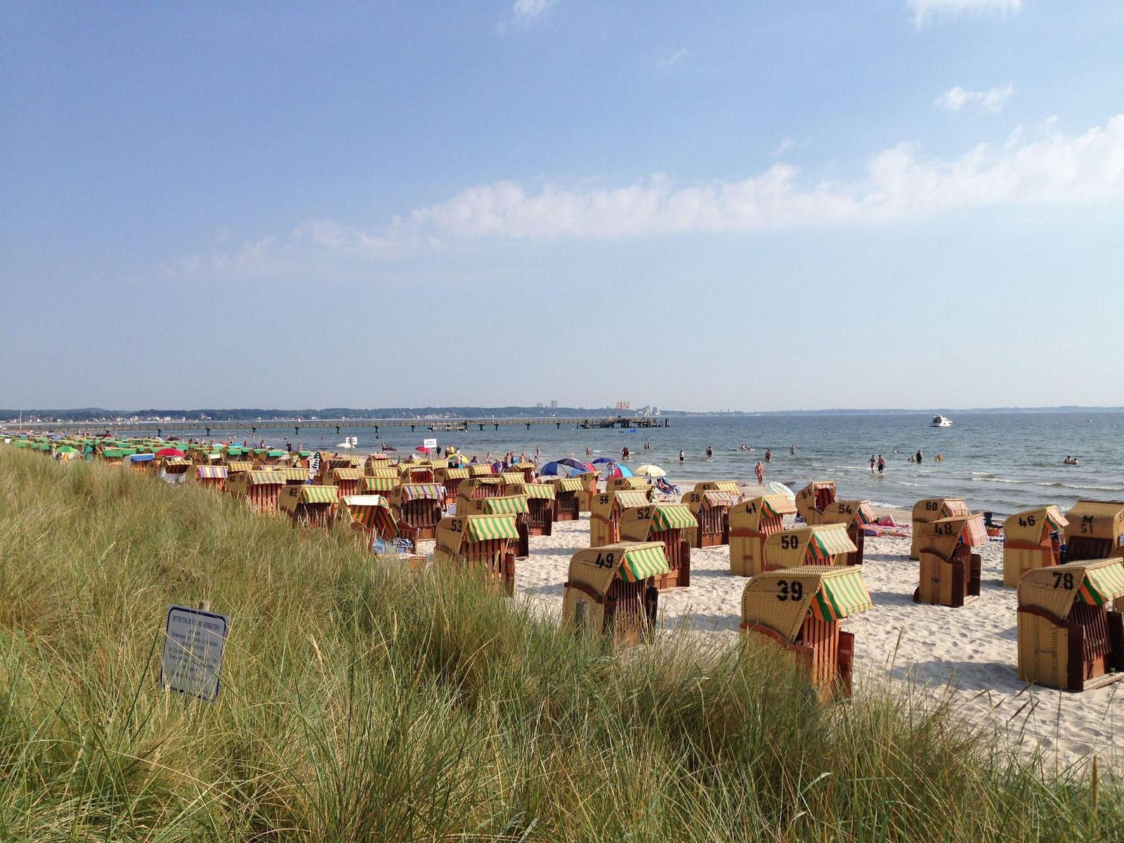Strand mit Strandkörben, Holzweg und Strandhütte unter blauem Himmel.