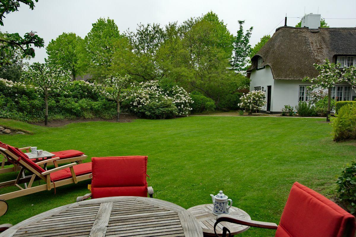 Red seating area in front of a white house with thatched roof and green lawn.