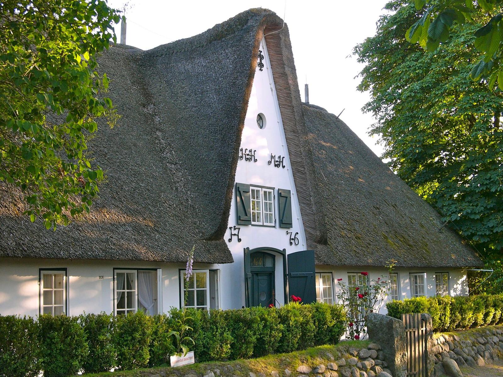 Red seating area with table in front of green lawn and house with thatched roof.
