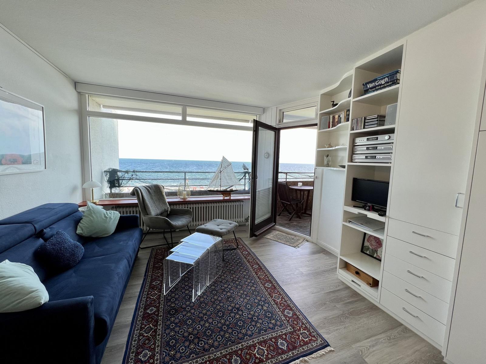 Schlafzimmer mit Bett, Esstisch und Küchenbereich. Wandbild mit roten Blumen.
