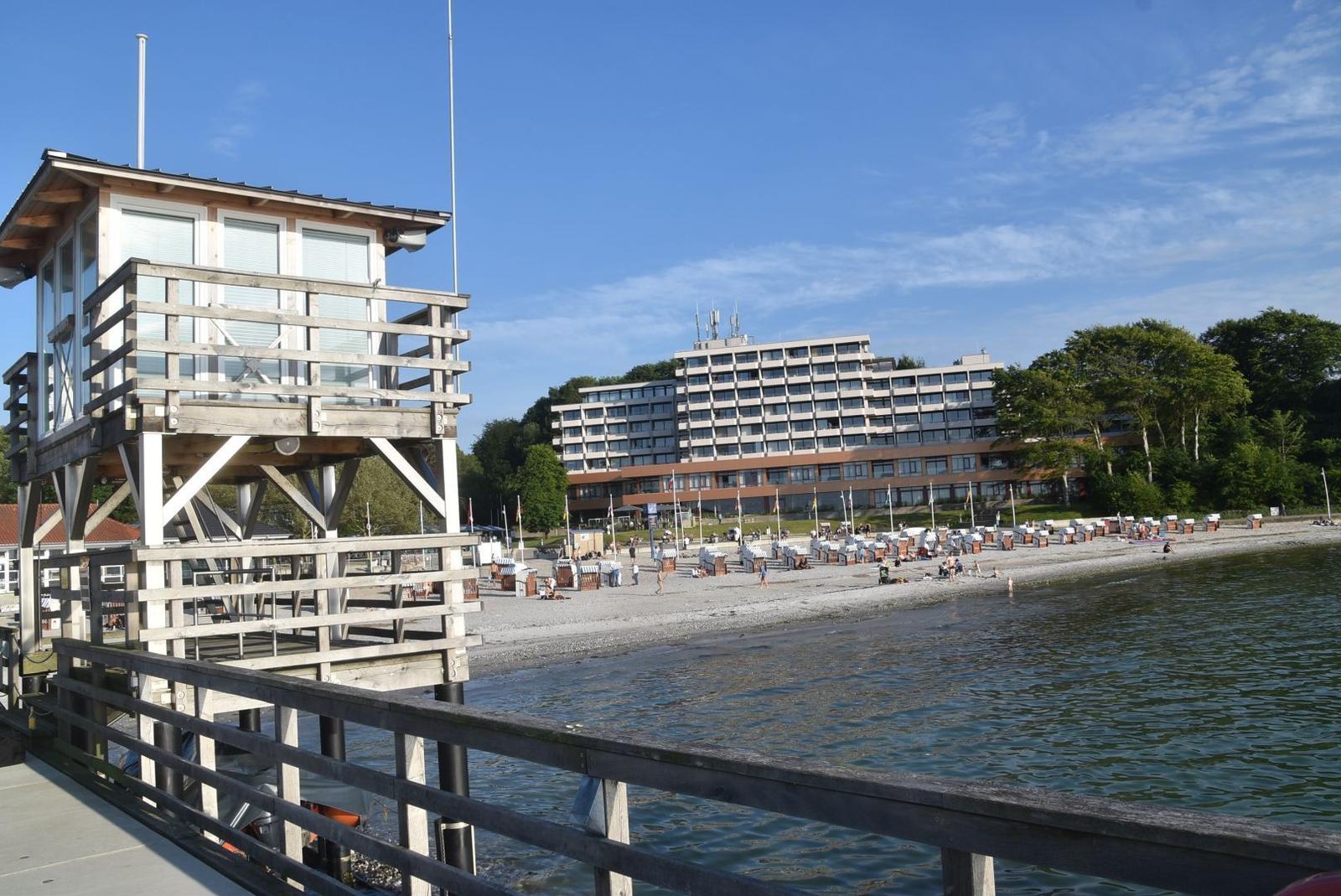 Strand mit Strandkörben und großem Hotelgebäude im Hintergrund.