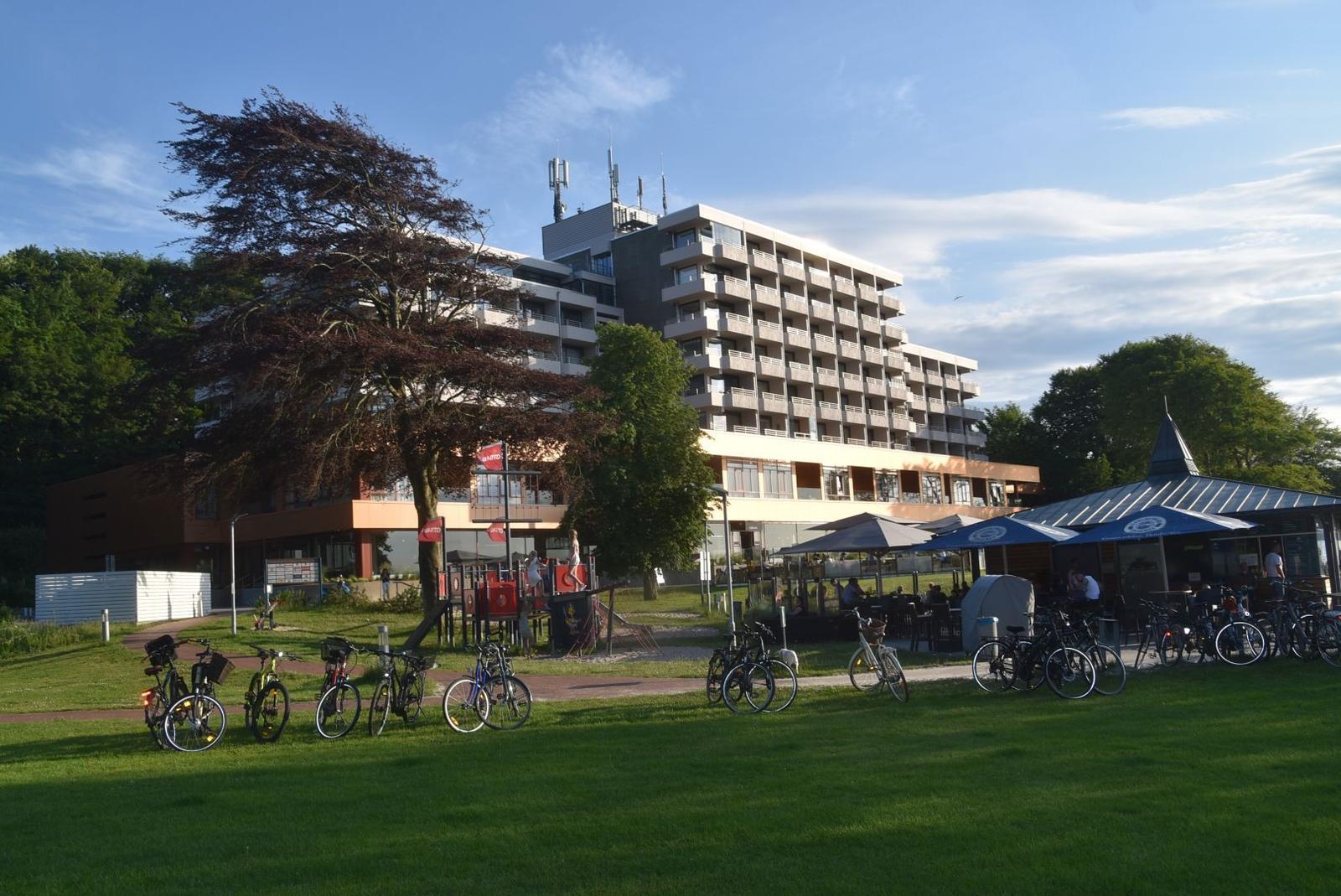 Strandpromenade mit Badekarren, Fahrrädern und historischem Schild an einem sonnigen Tag.