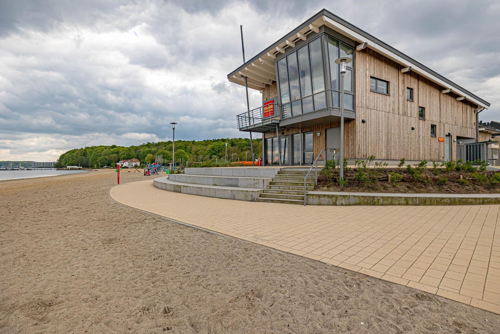 Strand mit Volleyballnetz und modernem Gebäude im Hintergrund.