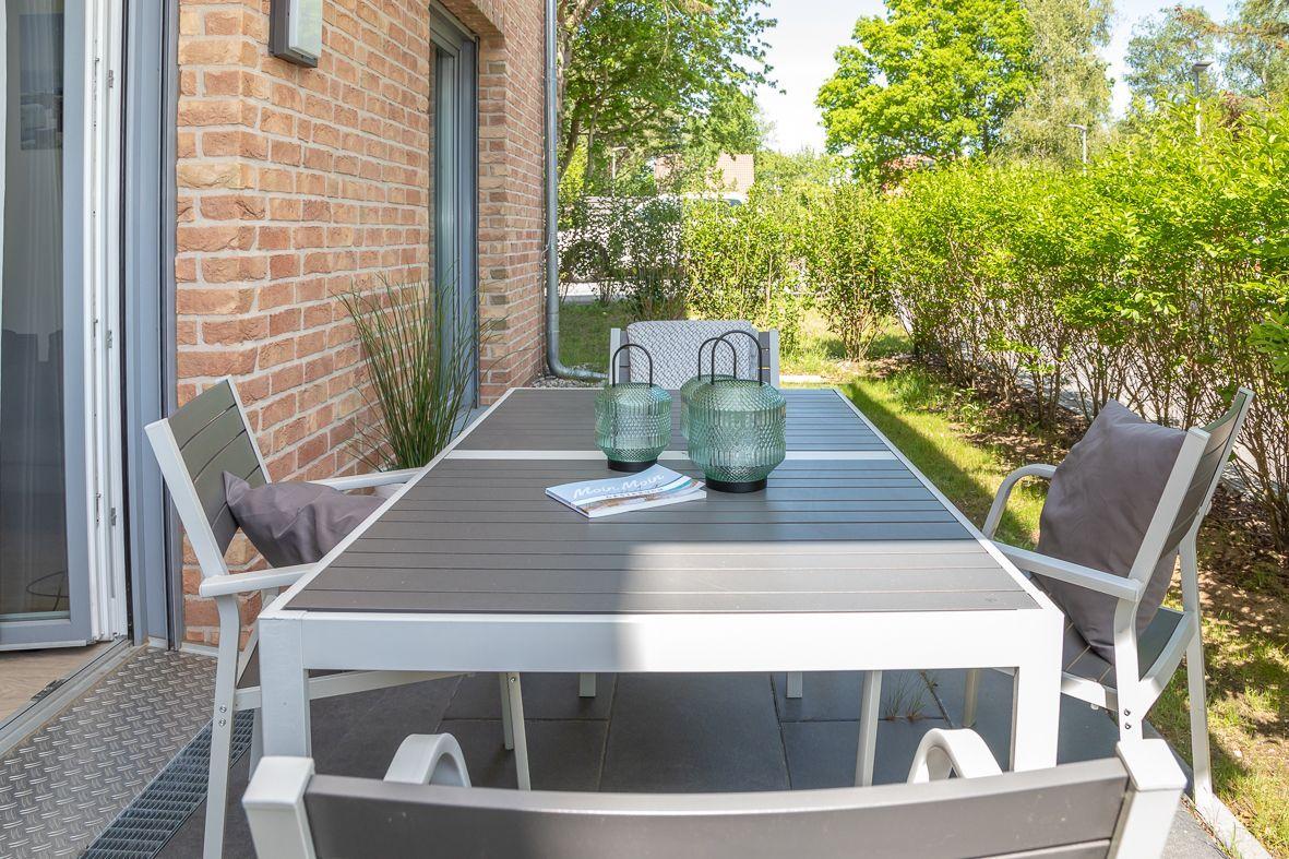 Terrasse mit Tisch, Stühlen und Pflanzen neben einem Haus mit Backsteinmauer.
