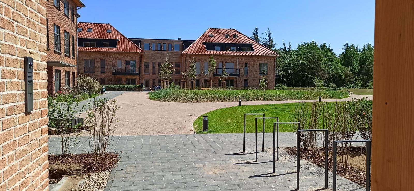 Holzspielplatz mit roter Rutsche und Klettergerüst auf grünem Rasen.