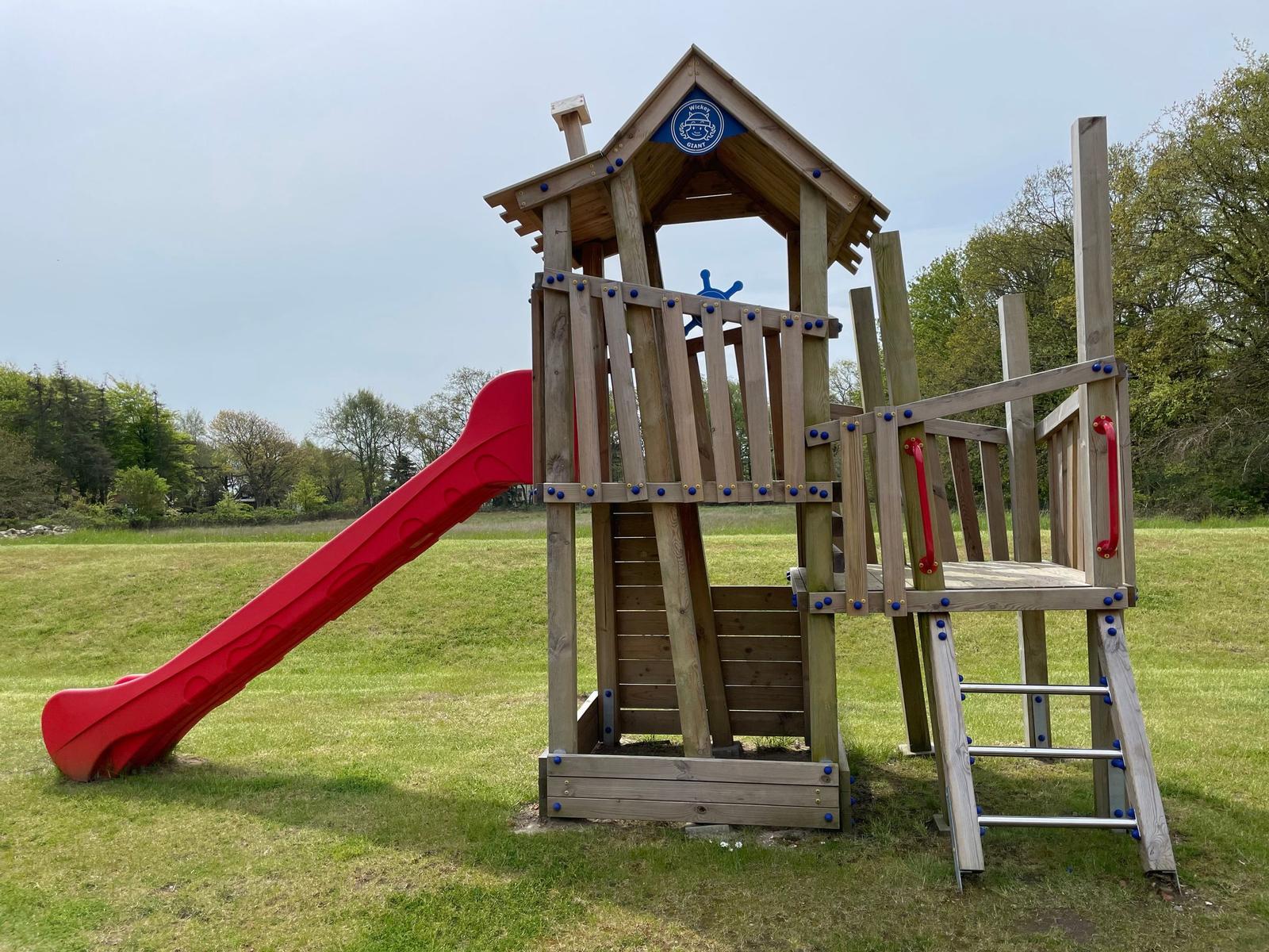 Großer Spielplatz mit Holzspielgerüst, Rutschbahn und Springtier auf grünem Rasen.