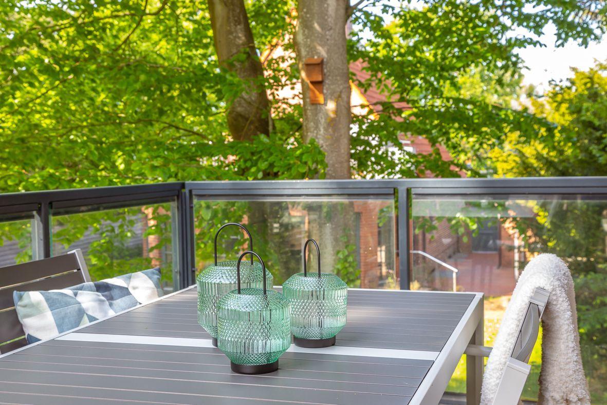 Terrasse mit Tisch und Stühlen, Blick in grüne Bäume durch Glasgeländer.